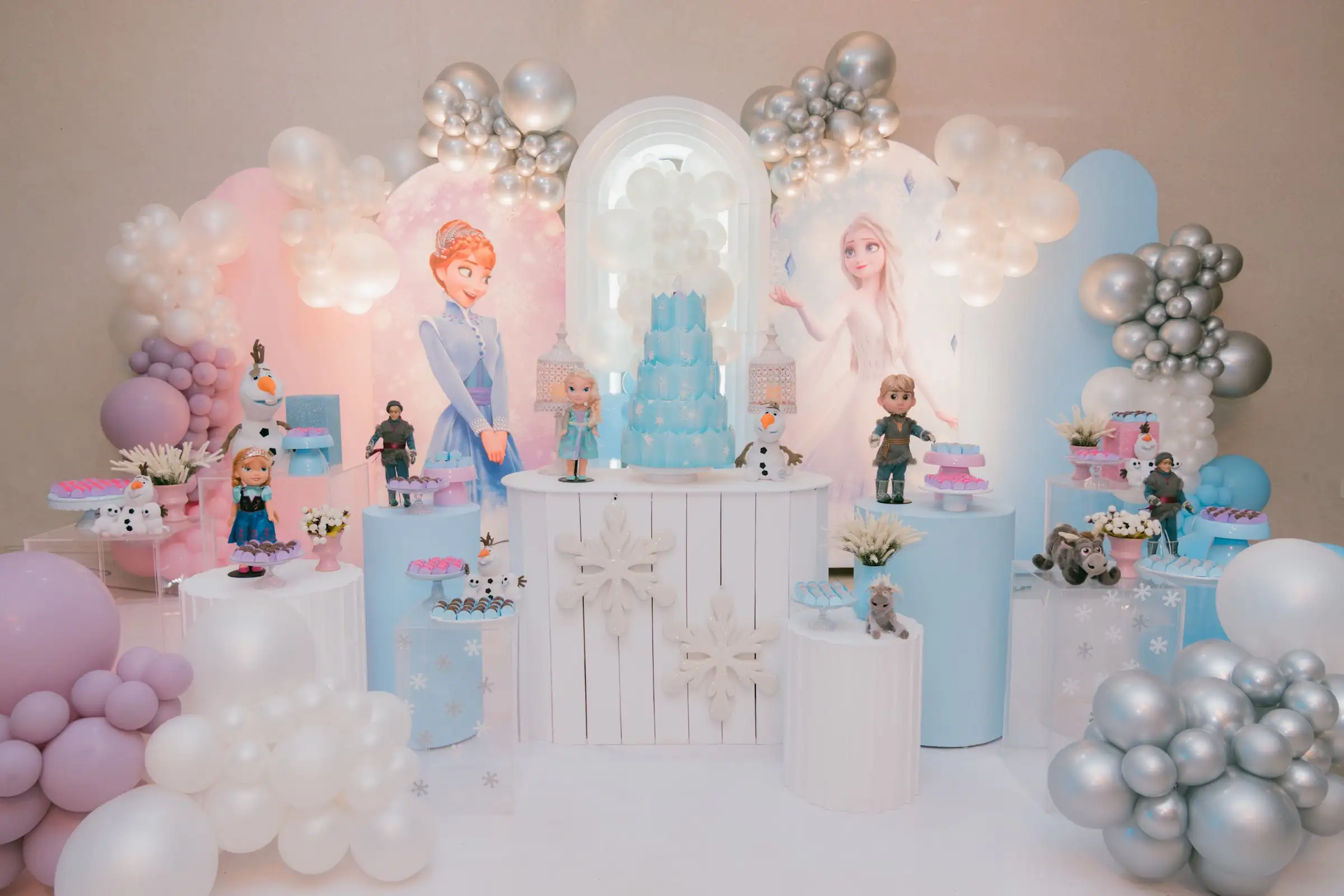 Painel com personagens de Frozen, bolo azul e balões em tons de rosa, lilás e prata