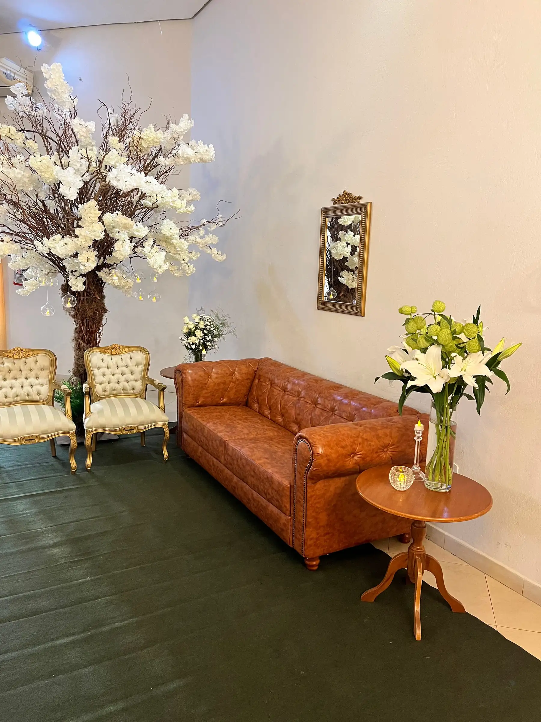 Lounge com sofá de couro caramelo, poltronas e árvore de flores brancas